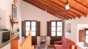 Uma sala de estar ampla com teto alto, vigas de madeira, um sofá vermelho, uma mesa de centro de vidro e uma lareira.