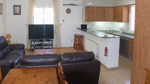 Sala de estar con televisor, sofá de cuero y mesa de centro de madera. Junto a ella, una cocina con gabinetes de madera, microondas y pileta.