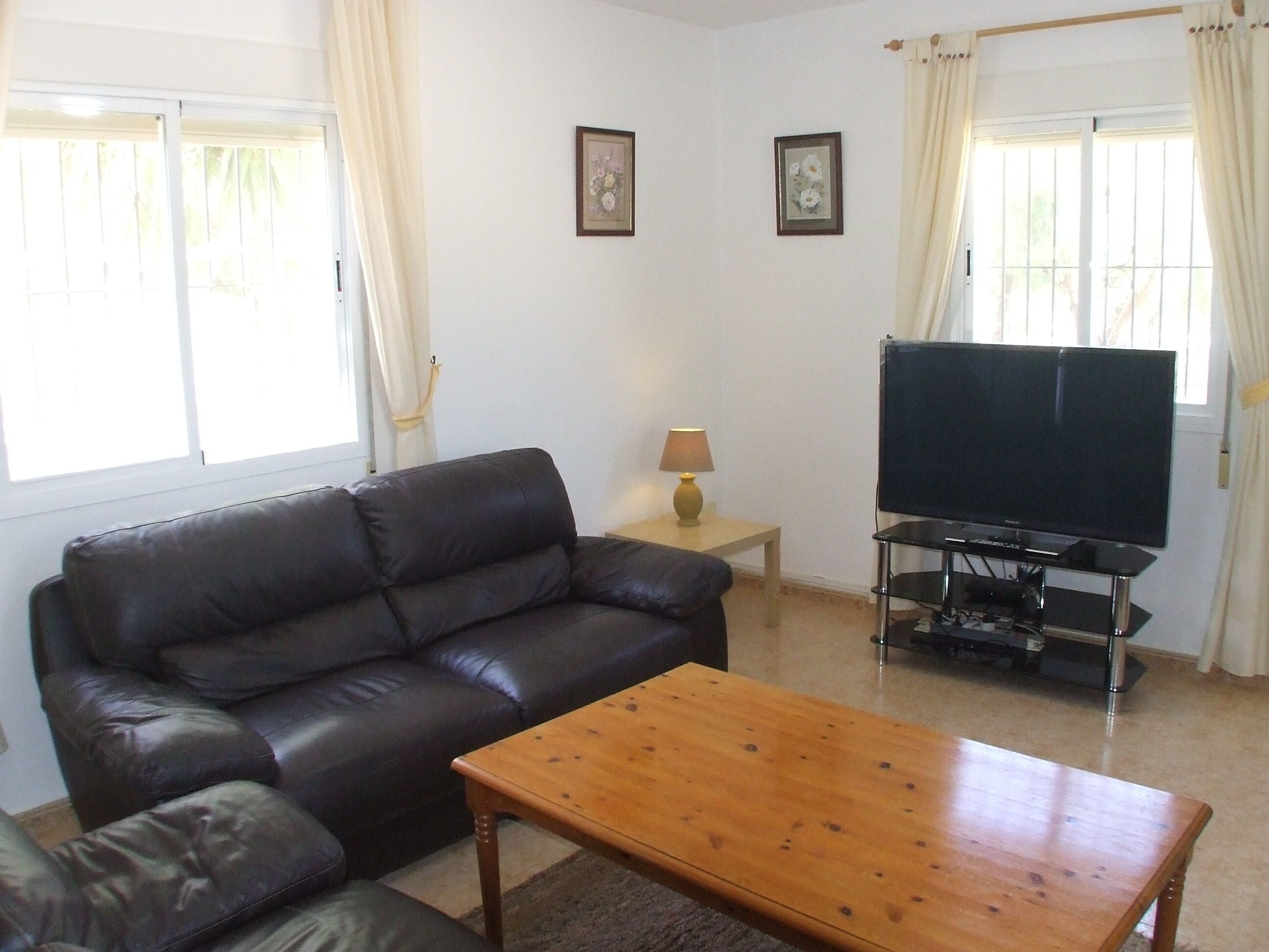 A living room with a leather sofa, a wooden coffee table, a TV on a stand, and two framed pictures on the wall.