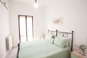 A bedroom with a bed, a radiator, a window, a bedside table, and a wall-mounted lamp. - APPARTAMENTI MARCIANA MARINA - APPARTAMENTO L'EDERA (Marciana Marina)