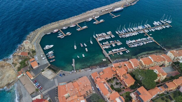 An aerial view of a marina with boats docked, a stone pier, and buildings with red-tiled roofs. - APPARTAMENTI MARCIANA MARINA - APPARTAMENTO L'EDERA (Marciana Marina)