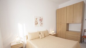A bedroom with a bed, nightstands, a wooden wardrobe, and a chair. - APPARTAMENTI MARCIANA MARINA - APPARTAMENTO L'EDERA (Marciana Marina)