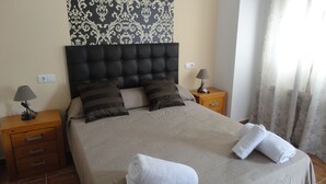 Een net opgemaakt bed met een donker hoofdbord, twee nachtkastjes met lampen, en een behang met patroon achter het bed.