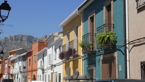 A row of colorful buildings with balconies, a clear blue sky, and mountains in the background. - 0533 Villa Laura Poblets (Denia)