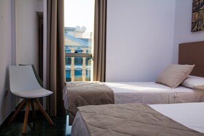 Ein Hotelzimmer mit zwei Betten, einem Sessel und Blick auf ein Gebäude mit blauen Fenstern.