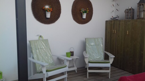 Dos sillas blancas con cojines a rayas verdes y blancas, una mesita con una taza verde y dos elementos decorativos en la pared con plantas.