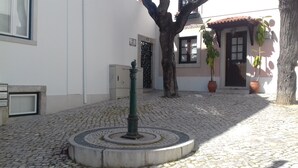 Un patio empedrado con un elemento circular central, un árbol y un edificio de techo con tejas y una puerta.