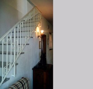 Eine Treppe mit weißen Balustern und einer Handläufe, die zu einer Empfangshalle mit einem Holzschrank und einem karierten Sofa führt.