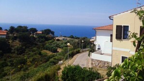 A coastal residential area with a white building featuring a red-tiled roof, surrounded by greenery and a clear view of the sea. - Il Fico holiday home (Colle D'Orano)