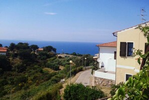 Ein Küstenwohngebiet mit einem weißen Gebäude, das ein rotes Ziegeldach hat, umgeben von viel Grün und freiem Blick auf das Meer.