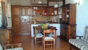 A kitchen with wooden cabinets, a dining table with chairs, and a plaid sofa. - Il Fico holiday home (Colle D'Orano)