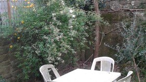Une table en plastique blanc et quatre chaises dans un jardin, avec un mur en pierre et des plantes en bambou.