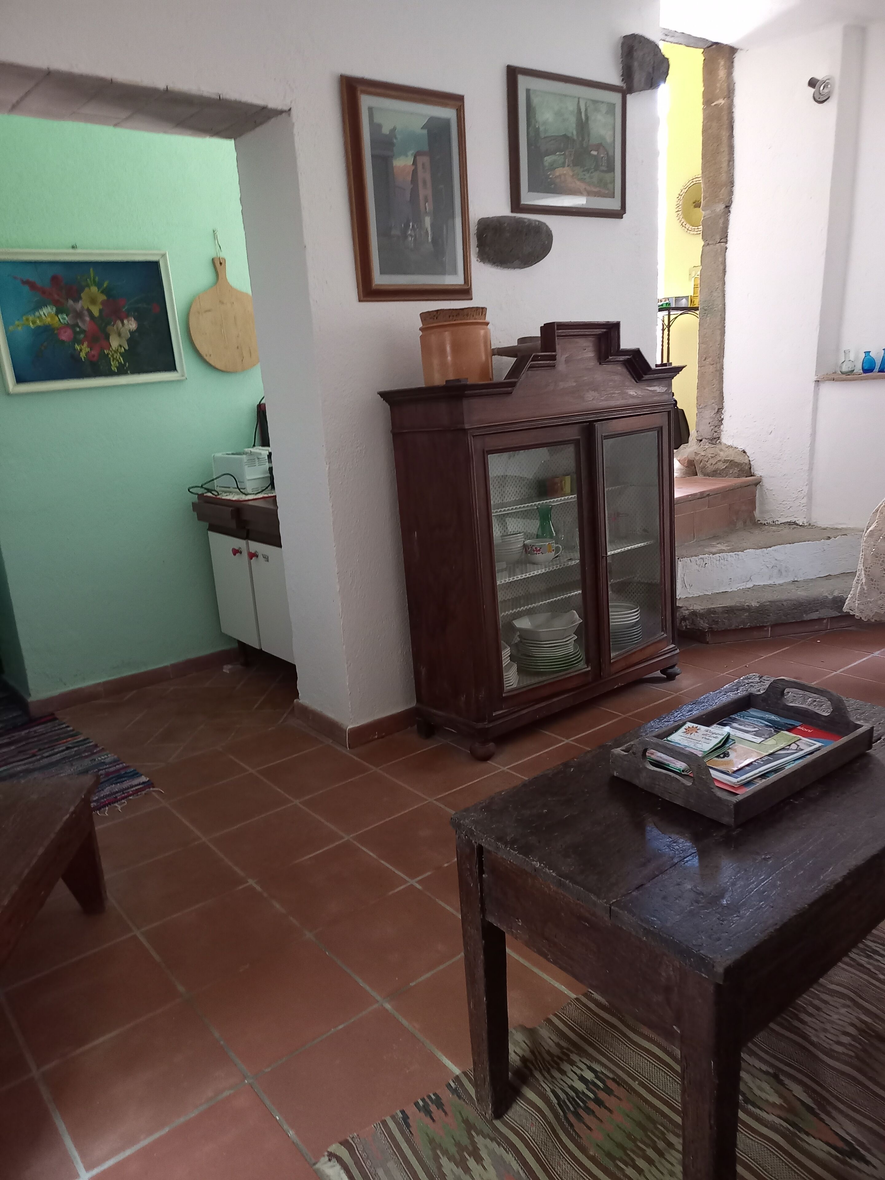 A living room with a wooden cabinet, a glass-fronted display case, and a tiled floor.
