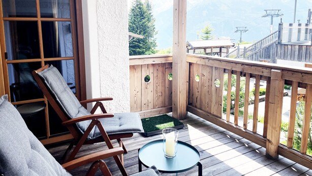 A wooden deck with a glass table and two wooden chairs, overlooking a mountainous landscape. - Luxury 2 bedroom apartment in Kitzbuhel Alps with private sauna (Mittersill)