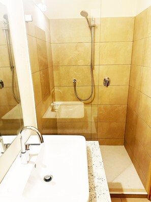Une salle de bain avec un lavabo blanc, une douchette à main et une cabine de douche séparée.