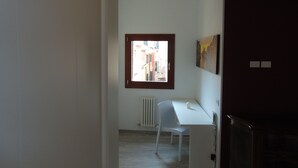 A room with a white desk, a white chair, a window with a view of buildings, and a radiator.