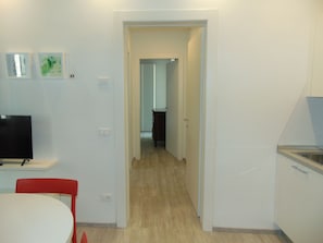 A modern kitchen with white cabinets, a built-in oven, and a microwave. A dining area with a white table and red chairs is visible.