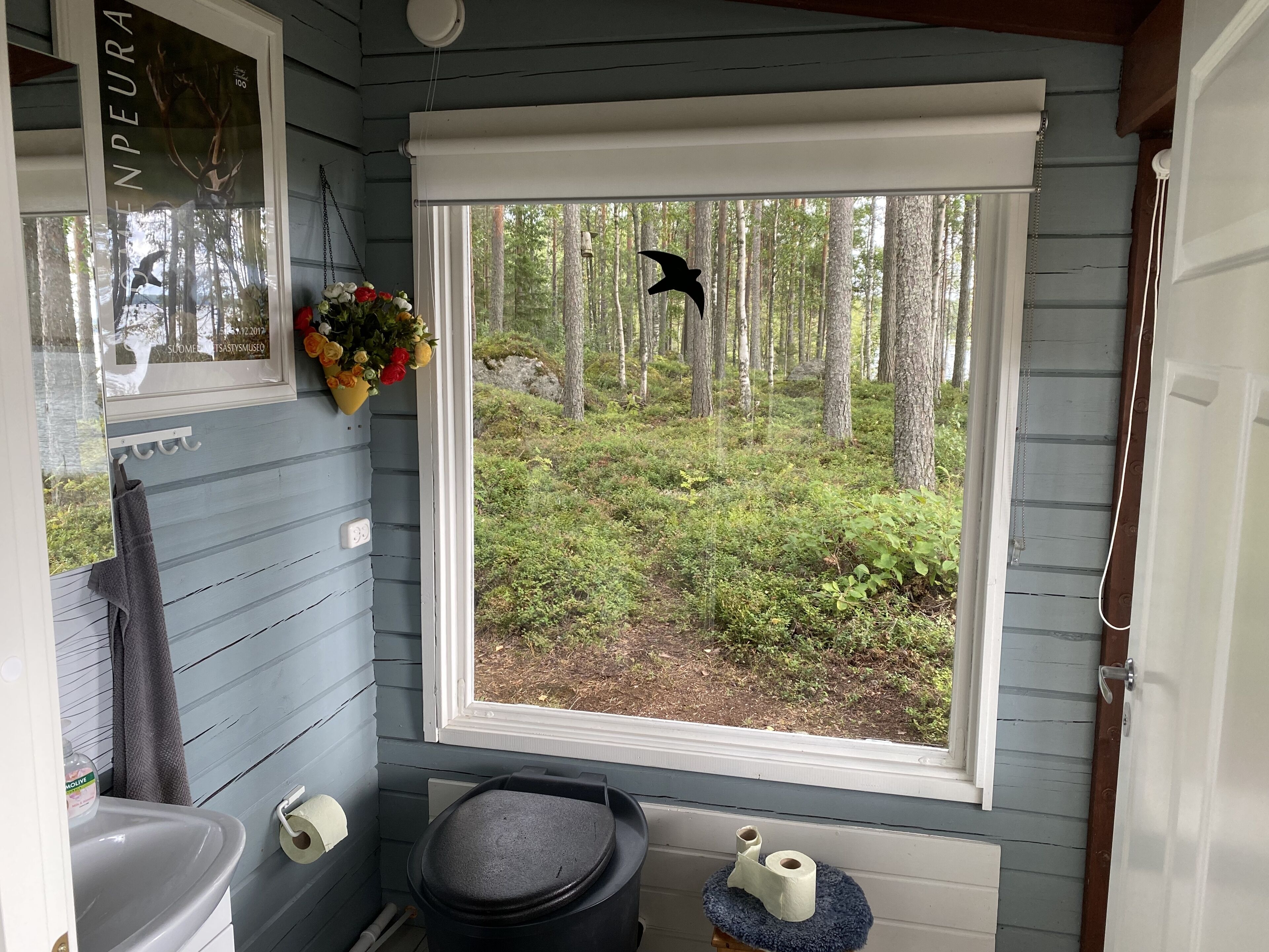 Une salle de bain avec une fenêtre donnant sur une forêt, un porte-serviettes, un lavabo et des toilettes.
