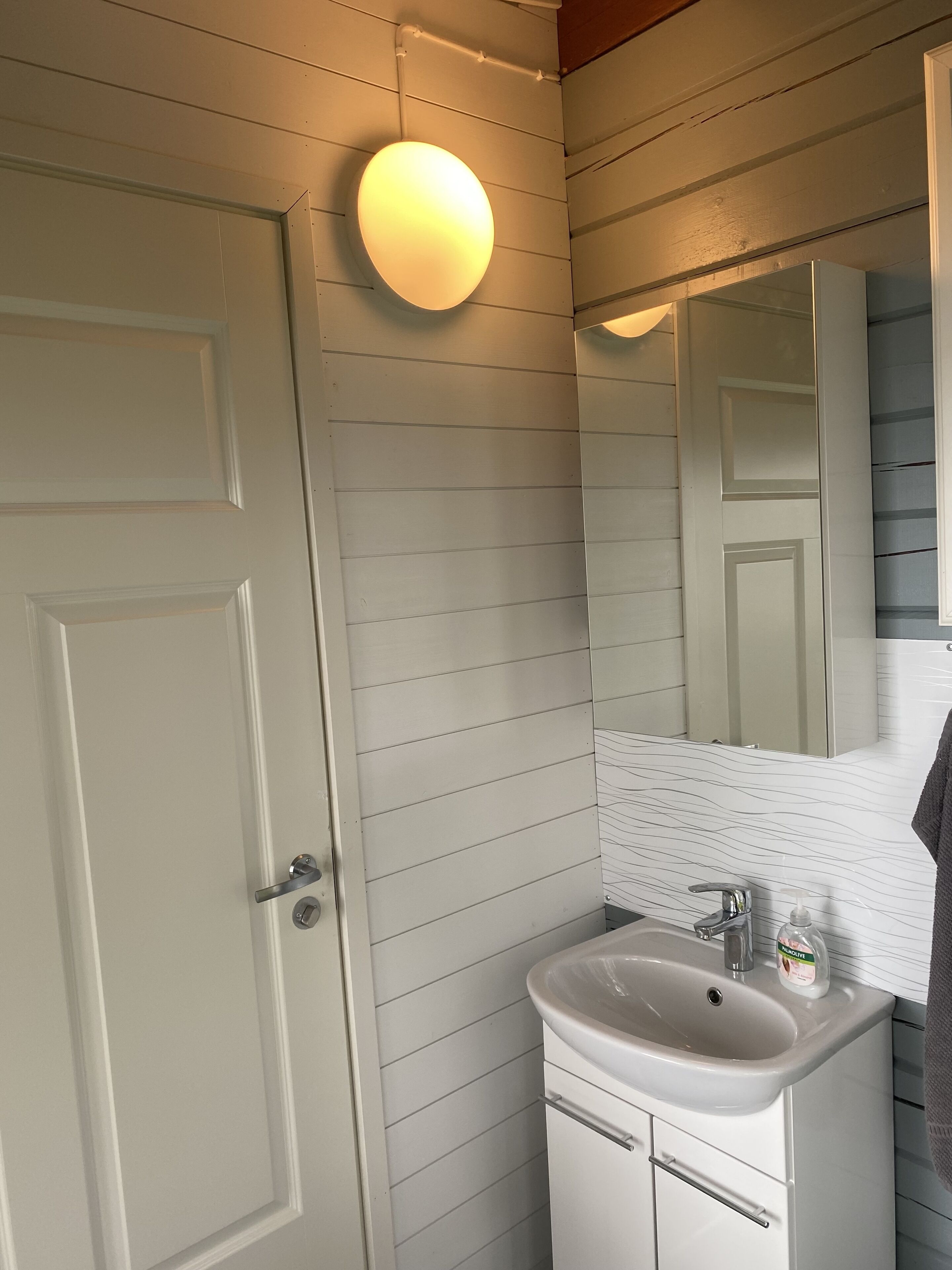 Un baño con paneles de madera blanca, un lavamanos blanco con un espejo encima y una toalla colgada a la derecha.