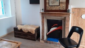 A room with a fireplace, a television mounted on the wall, a wooden cabinet, and a black chair. - Pretty fisherman's house (Ault)