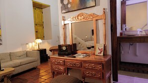 Une pièce comprenant une commode en bois, un miroir, un canapé, une lampe et une fenêtre avec un rideau.