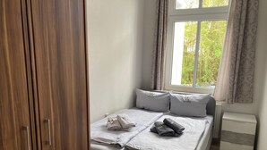 A neatly made bed with pillows and towels, a window with curtains, a radiator, and a wooden wardrobe. - Rosenbogen - Holiday apartment with conservatory and terrace (Wangerooge)