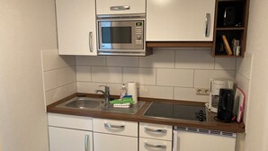 A kitchen with white cabinets, a stainless steel microwave, a sink, and a coffee maker. - Rosenbogen - Holiday apartment with conservatory and terrace (Wangerooge)