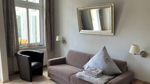 A living room with a sofa, a chair, a lamp, a mirror, and a window with curtains. - Rosenbogen - Holiday apartment with conservatory and terrace (Wangerooge)