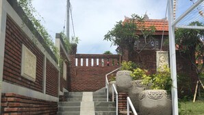A staircase leading up to a building with a brick wall and a metal railing. - Oka's Guest House (Canggu)
