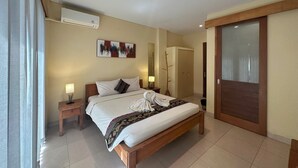 A hotel room with a bed, bedside tables, a wardrobe, and a large window. - Oka's Guest House (Canggu)