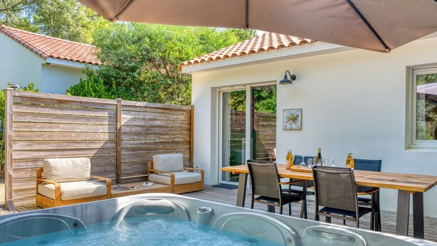 A hot tub with seating, a table with chairs, and a patio umbrella. - Villa Brésil - Domaine Le Sherwood (Notre-Dame-De-Monts)