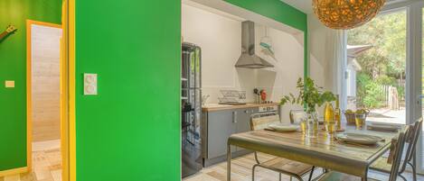 Une cuisine moderne avec un mur vert, un coin repas avec une table et des chaises, et une vue sur l’extérieur.