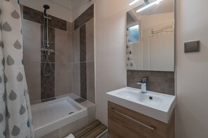 Un baño con ducha, lavamanos y espejo.