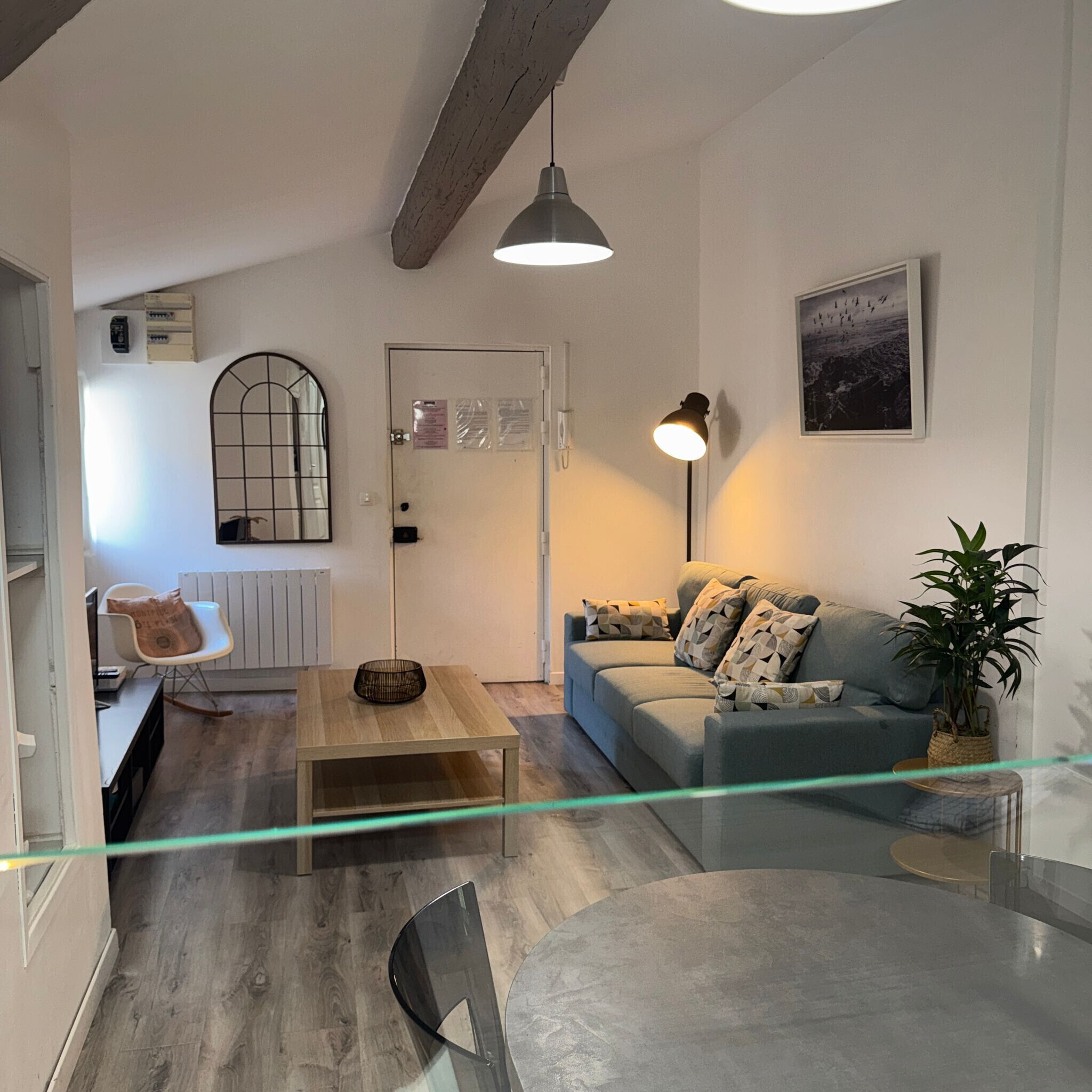 Uma sala de estar moderna com um sofá, uma mesa de centro, uma poltrona e um abajur. Há uma porta com janela e um radiador.