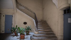 A spiral staircase with a wrought iron railing, potted plants at the base, and a blue door to the left.