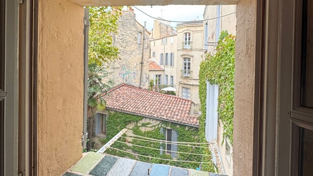 A window with a view of a courtyard with buildings and a tiled roof.