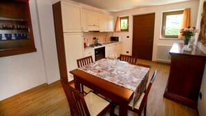 Een compacte keuken met witte kastjes, een magnetron en een spoelbak. Er staat een eettafel met stoelen en een vaas met bloemen ernaast.