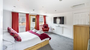 Una camera d'albergo con un letto, una televisione, una poltrona rossa e una grande finestra.