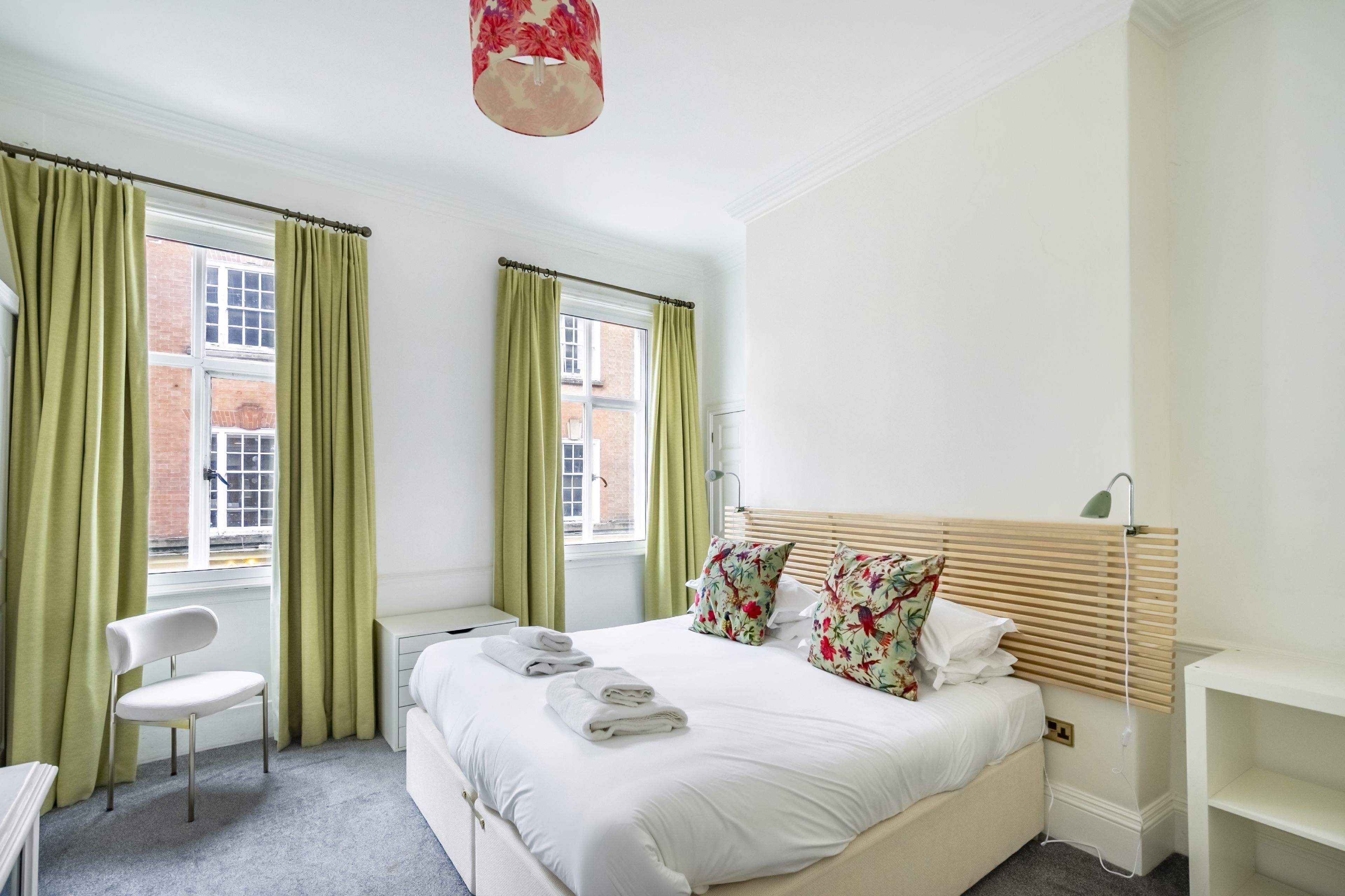 Une chambre d’hôtel avec un lit, une chaise, un bureau et une fenêtre avec des rideaux.