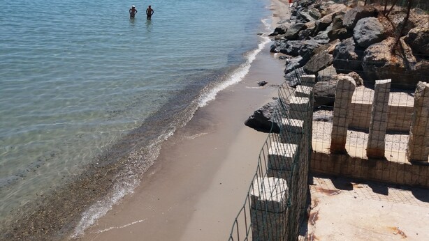 Uma praia com águas cristalinas, costa rochosa e uma área cercada.
