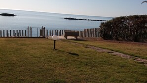 Área gramada com um banco e uma cerca, com vista para um corpo d'água calmo.