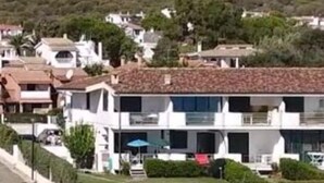 Zona residencial costeira com casas modernas, vista clara para o mar e uma encosta ao fundo.