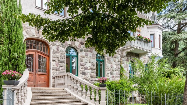 Un edificio in pietra con una porta d'ingresso in legno, una scala che conduce a un balcone e un recinto metallico.
