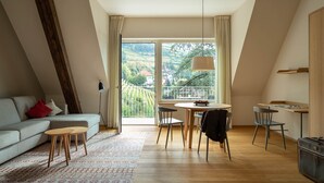 Un soggiorno moderno con divano, tavolo da pranzo e sedie. Una grande finestra offre vista su un paesaggio collinare.