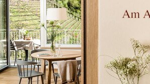 Zona pranzo con tavolo rotondo, sedie e vista su un giardino attraverso ampie finestre.