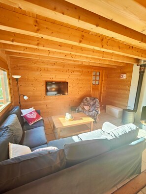 A cozy wooden cabin interior with a sofa, a table with a decorative item, a television, and a fireplace.