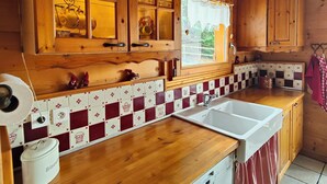 A wooden kitchen with a large window, a sink, and cabinets. - Authentic, cosy chalet for an ideal family holiday (Briançon)
