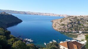 A coastal town with boats docked at a marina, surrounded by hills and clear blue water.