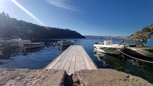 A wooden dock with boats moored on either side, a clear sky, and a hilly landscape in the background.