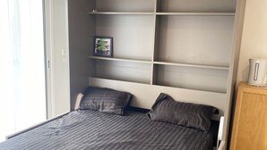 Een slaapkamer met een bed, inbouwkasten, een kastje en een deur.